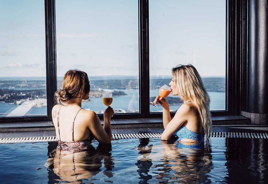 Fotografi av två personer som står i en pool. Båda personerna håller i varsitt glas.