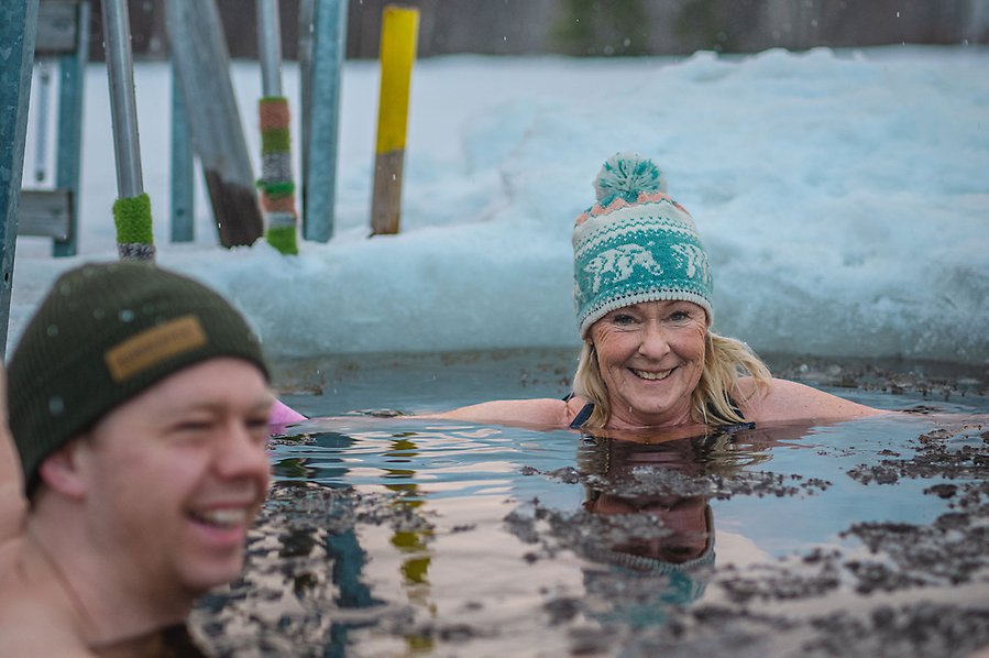 Fotografi av två personer som badar i en isvak. Båda personerna ler. 